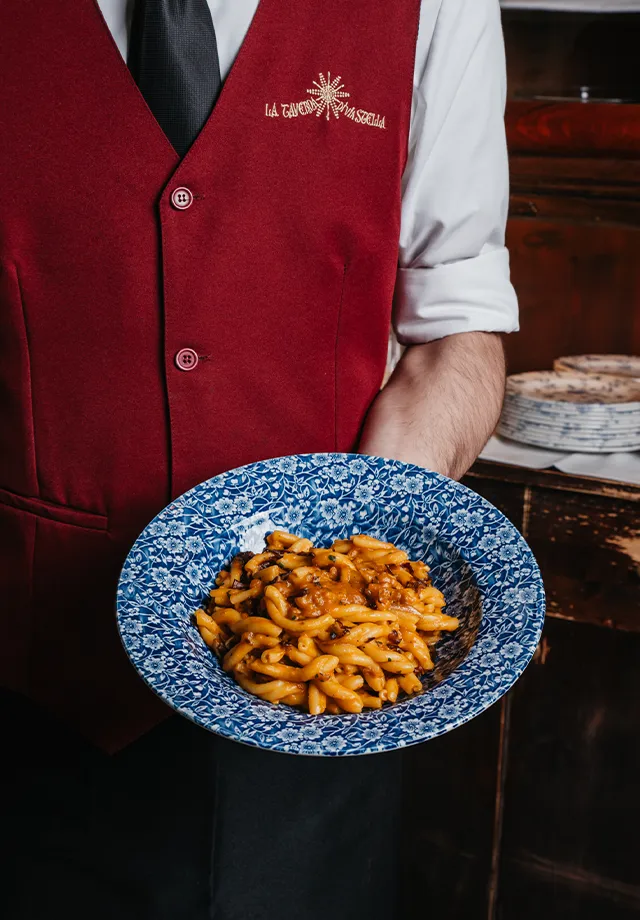 Cameriere serve un piatto di casarecci con zucca, radicchio e tastasal