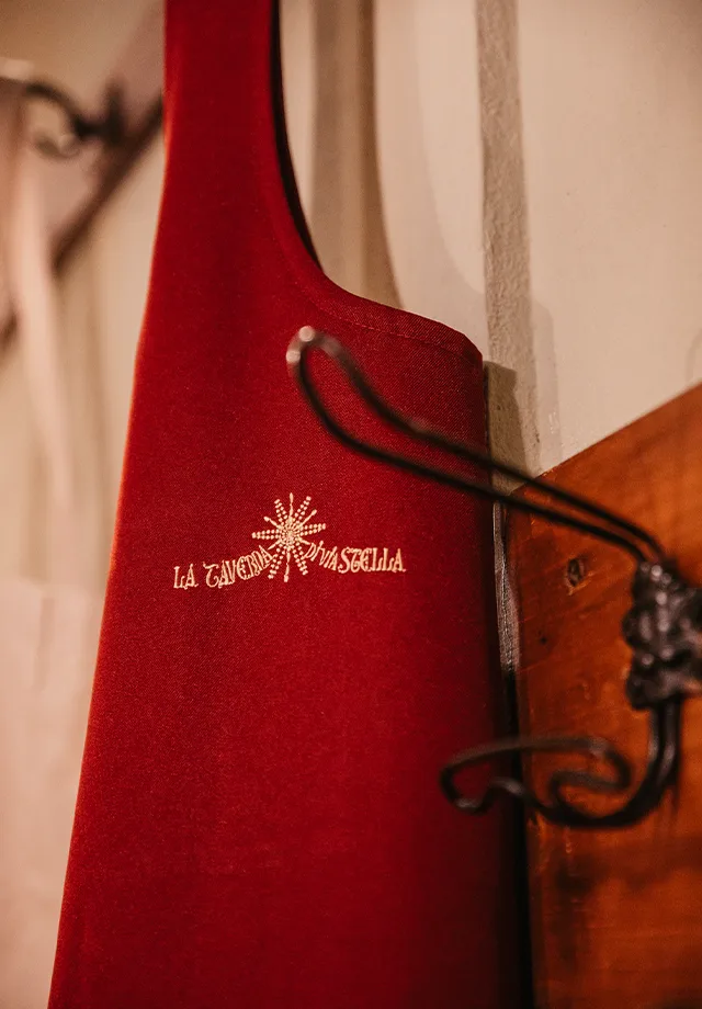 Dettaglio dei grembiuli rossi indossati dal personale di sala con il logo della taverna ricamato in colore oro