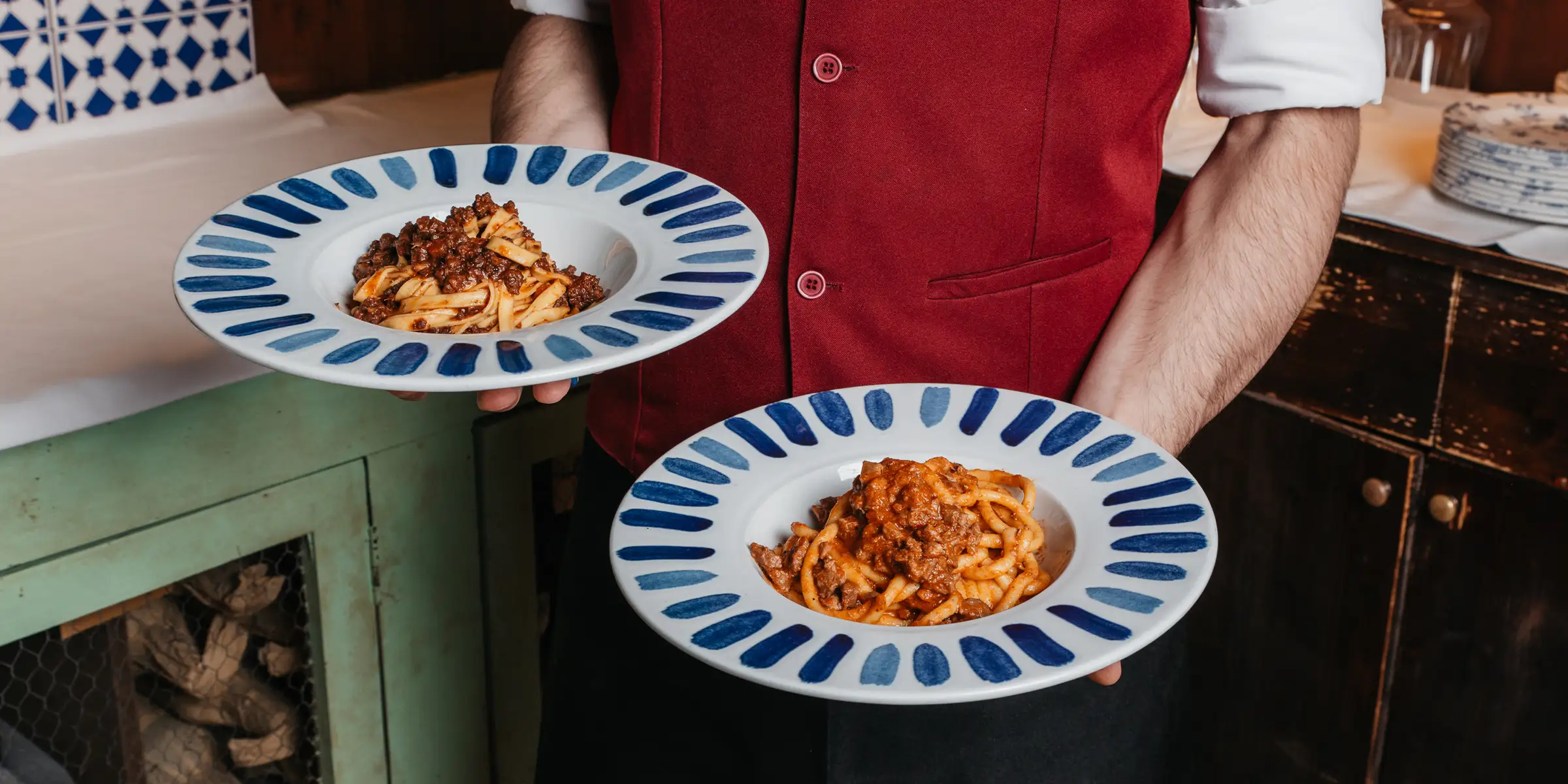 Cameriere tiene in mano due piatti di pasta per un tavolo